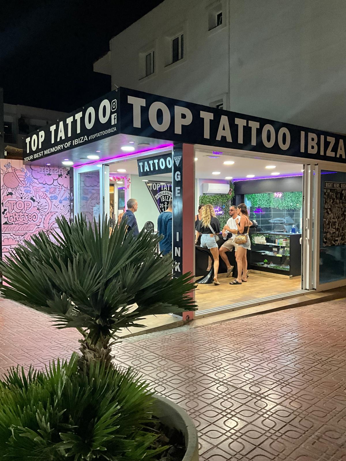 Top Tattoo Ibiza storefront at night in Platja d'en Bossa — neon-lit entrance, palm in foreground