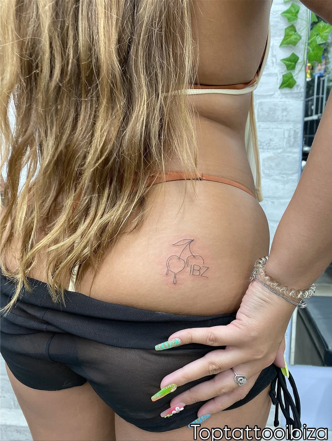 Fine-line cherries and 'IBZ' lettering tattoo on a hip