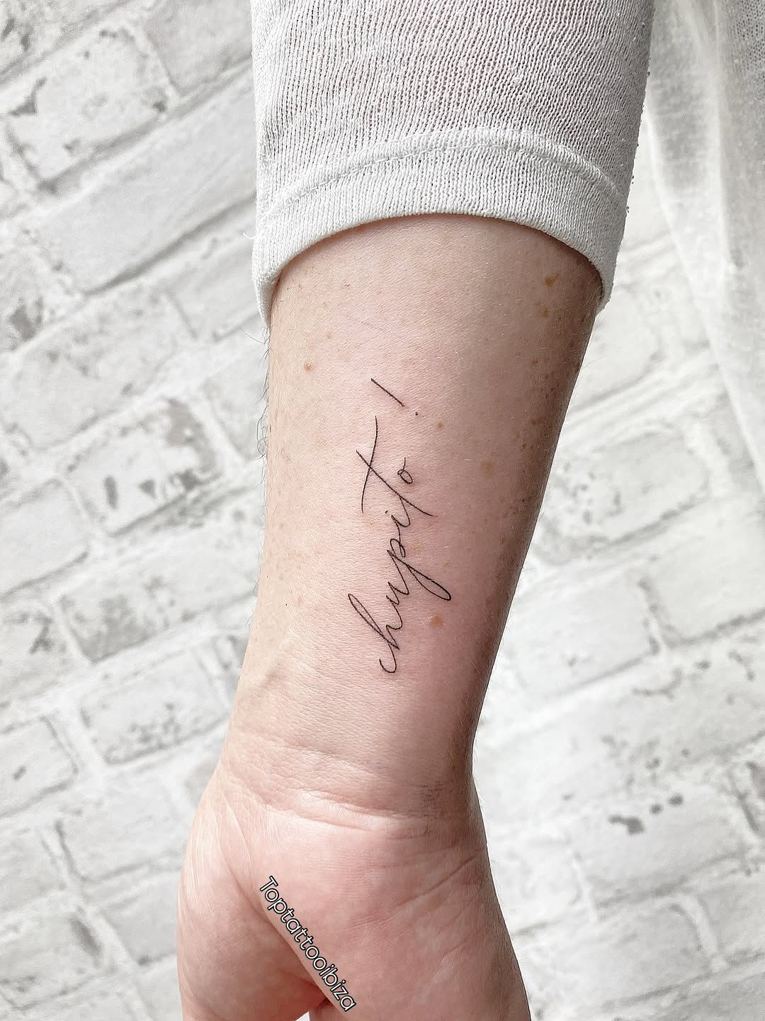 Fine-line script tattoo reading 'chupito!' on inner arm